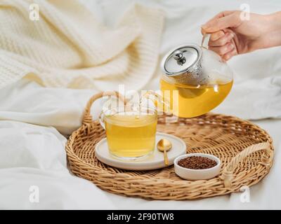 Thé de sarrasin ou kuqiaocha. Thé de soba sain dans une tasse de verre, et théière en verre, géliats dans un petit bol et miel sur plateau rond tressé en rotin sur blanc être Banque D'Images