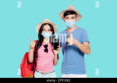 Jeune couple dans des masques de visage et montrant le téléphone mobile pour voyagez en été Banque D'Images