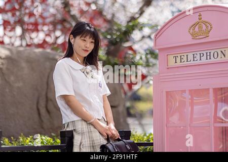 Huzhou, Chine 22 Mars 2021: Portrait extérieur de la belle jeune fille chinoise dans l'uniforme de l'école de style japonais souriant près du brunch de cerisier de fleur Banque D'Images