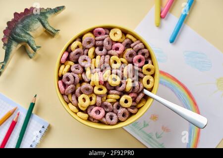 Vue de dessus des cornflakes multicolores dans un bol sur le fond du dessin des enfants et des jouets. Banque D'Images