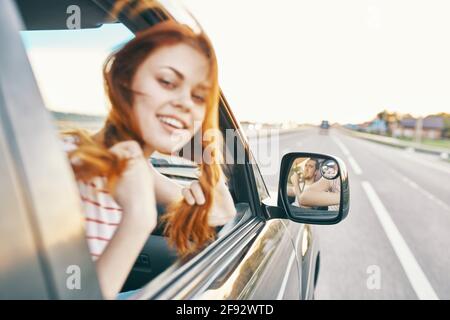 bonne femme aux cheveux rouges regarde par la fenêtre de la voiture et conduit sur la route, piste des vacances d'été Banque D'Images