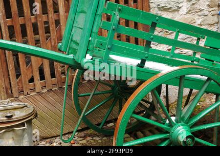 vieux chariot en bois vert avec de la neige sur des pavés anciens en face de l'ancien mur en pierre avec porte en bois et à côté de vieux poubelle en métal Banque D'Images