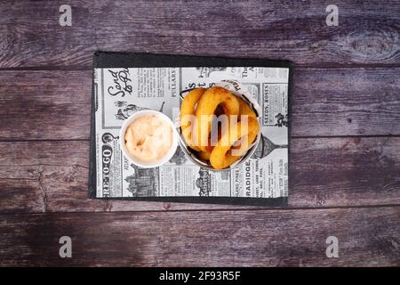 Cuits au four, les rondelles de calmar panées sont servies avec de la sauce douce et de la mayonnaise, sur fond de table en bois Banque D'Images