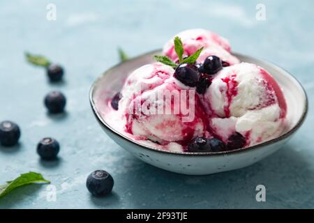 Yaourt maison et glace aux myrtilles avec sirop de myrtille naturel dans un bol sur fond bleu rugueux Banque D'Images