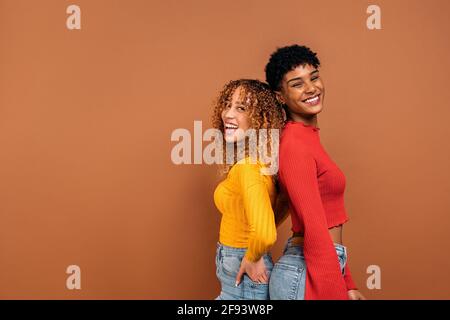 Photo de femmes afro gaies posant en studio sur fond marron. Banque D'Images