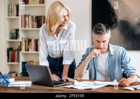 Réunion des partenaires commerciaux. Deux collègues d'affaires caucasiens matures et confiants travaillant ensemble à la table dans un bureau moderne, discutant des idées d'affaires, regardant à travers les documents, développant une stratégie Banque D'Images