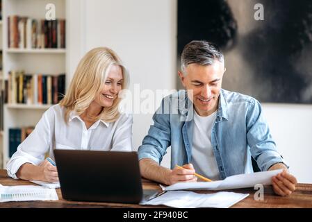 Homme d'affaires et femme d'affaires en vêtements élégants sont assis à la table, parler, travailler sur un nouveau projet, regarder et vérifier des documents, faire des modifications, développer la stratégie, sourire Banque D'Images