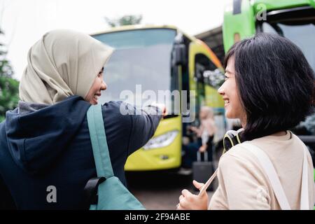 une femme dans un foulard avec un doigt pointant vers le bus tout en parlant à une femme avec des écouteurs Banque D'Images