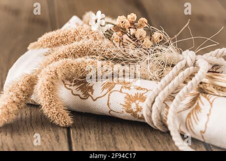 Serviette en papier roulée ou torchon à vaisselle décorée de fleurs séchées et d'un ruban, décoration de table aux couleurs naturelles sur une table en bois Banque D'Images