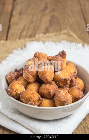 Mutzen ou Castagnole maison, beignets de carnaval typiquement allemand ou italien avec sucre dans un bol blanc sur une table rustique en bois, vertical avec espace de copie Banque D'Images