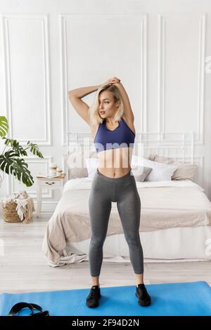 La femme sportive blonde-cheveux s'étire avant l'exercice, s'entraîner le matin à la maison. Belle jeune femme fait l'échauffement avant l'entraînement Banque D'Images