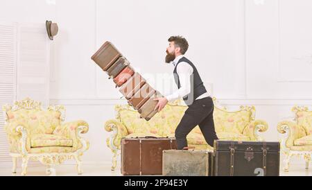 Concept d'assurance bagages. Homme avec barbe et moustache en costume classique livre des bagages, luxe intérieur blanc arrière-plan. Porter, maître d'hôtel accidentellement Banque D'Images