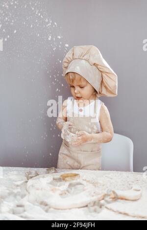 un enfant heureux dans un tablier et un chapeau de chef prépare de la pâte, fait cuire des biscuits dans la cuisine Banque D'Images