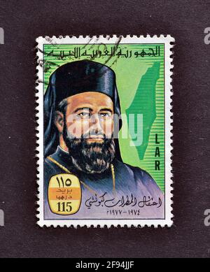 Timbre-poste annulé imprimé par la Libye, qui montre le portrait de l'archevêque Hilarion Capucci et la carte de Palestine, vers 1977. Banque D'Images