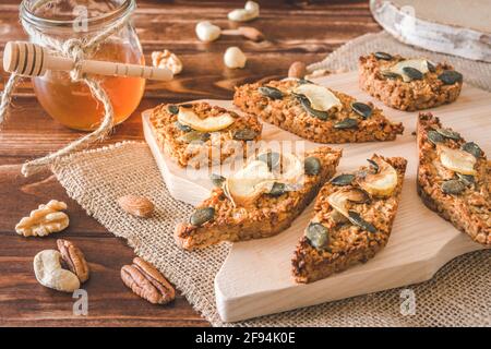 Barres de granola aux pommes faites maison, décorées de graines de pomme et de citrouille séchées, couchées sur une latte en bois sur fond de bois Banque D'Images