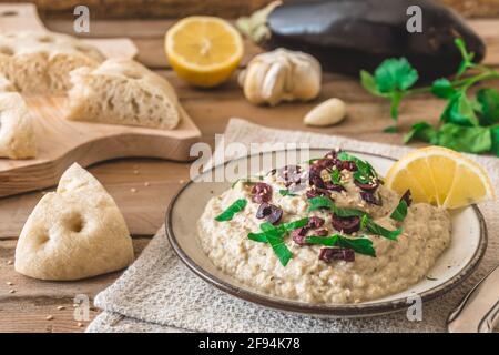 Cuisine arabe : Baba Ganoush aux olives noires et au persil haché et au pain plat sur une table rustique en bois Banque D'Images