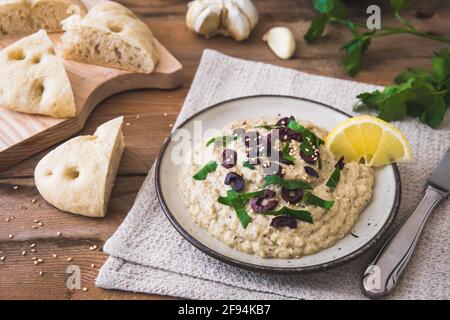 Cuisine arabe : Baba Ganoush aux olives noires et au persil haché et au pain plat sur une table rustique en bois Banque D'Images