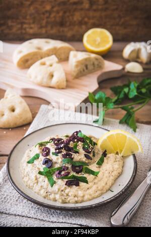Cuisine arabe : Baba Ganoush aux olives noires et au persil haché et au pain plat sur une table rustique en bois. Verticale Banque D'Images