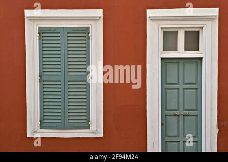 Façade de maison néoclassique avec une porte en bois taillée de blanc et des volets de fenêtre sur un mur en stuc rouge vénitien dans l'île de Syros, Cyclades Sud Egée, G. Banque D'Images