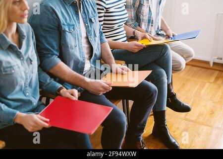 Vue rapprochée des jeunes assis dans des chaises avec des dossiers avant l'entrevue d'emploi dans la salle d'attente. Banque D'Images