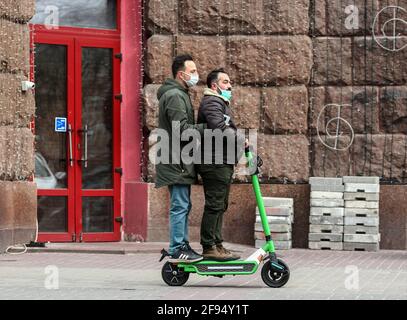 Les hommes portant des masques de protection contre la propagation du coronavirus COVID-19 sont équipés d'un scooter électrique dans la rue.depuis que la situation épidémique du coronavirus Covid-19 dans la capitale ne s'améliore pas de manière significative, les autorités ont prolongé la quarantaine à Kiev jusqu'en avril 30, a déclaré le maire de Kiev, Vitali Klitschko. Les restrictions précédemment introduites seront en vigueur dans la ville jusqu'en avril 30. Toutes les écoles et jardins d'enfants restent fermés, tous les transports publics - le sol et le métro travaillent exclusivement avec des laissez-passer spéciaux, les établissements de restauration ne fonctionnent que pour les plats à emporter Banque D'Images