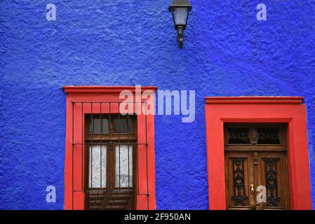 Façade de maison coloniale avec un mur texturé bleu cobalt et une fenêtre et porte rouge écarlate à Santiago de Querétaro, Mexique. Banque D'Images