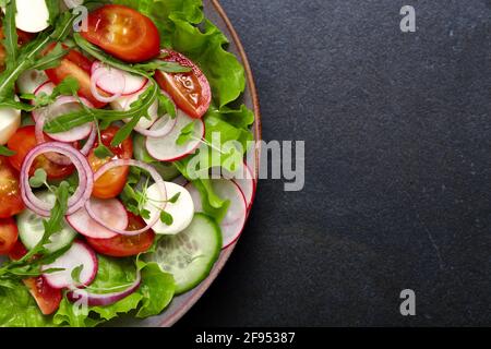 Salade fraîche saine avec radis, concombre, tomate cerise et mozzarella sur fond sombre. Plats faits maison. Banque D'Images