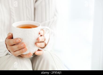 Les mains de la femme tiennent une tasse chaude de café ou de thé au soleil du matin. Banque D'Images