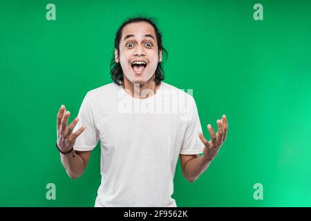 Portrait d'un jeune homme avec de longs cheveux noirs avec une expression de bonheur choquée tout en faisant monter les paumes ouvrir Banque D'Images