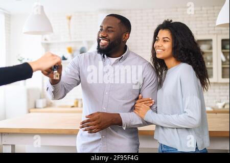 Concept d'achat d'une nouvelle maison. Le couple heureux prend les clés de leur nouvelle maison de courtier et souriant. Mains de l'agent immobilier donnant les clés au couple. L'agent a remis les clés à un jeune couple Banque D'Images