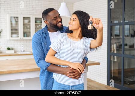 Le jeune africain américain heureux couple marié, homme embrasse belle femme qui tient les clés de l'appartement, concept de déménagement dans une nouvelle maison, acheté avec un prêt hypothécaire, les rêves deviennent réalité, nouveau niveau Banque D'Images