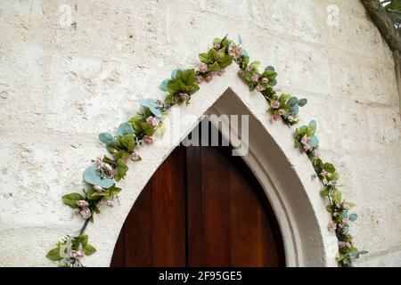 Une porte médiévale à l'ancienne légèrement entrouverte à la Barbade, entourée de vignes grimpantes de lierre verte avec des fleurs et une église coloniale à l'ancienne. Banque D'Images