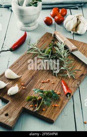 Herbes, ail, piment et couteau sur une latte en bois rustique brun, avec mortier sur une table en bois gris rustique. Verticale. Banque D'Images