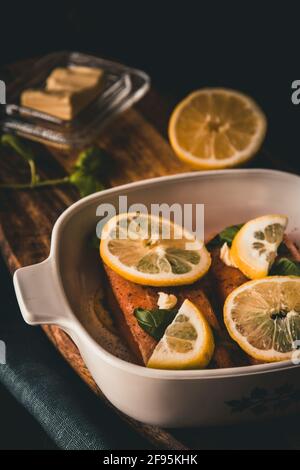 Deux morceaux de saumon cru, couverts de beurre, de basilic et de tranches de citron dans une casserole. Verticale. Banque D'Images