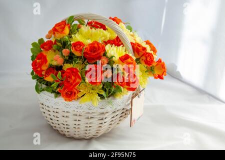 Bouquet de fleurs panier en osier, avec roses rouges et chrysanthèmes jaunes dans boîte cadeau. Gros plan, fond blanc Banque D'Images