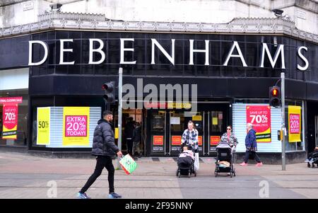 Les gens marchent devant un magasin Debenhams à Manchester, dans le Grand Manchester, en Angleterre, au Royaume-Uni, qui affiche des affiches de vente de clôture. Debenhams a rouvert des dizaines de ses magasins de grande rue en avril 2021 pour une fermeture de stock avant la fermeture finale le 15 mai. Le grand magasin, qui s'est effondré en 2020, offre jusqu'à 70 % de rabais sur ses stocks. Le verrouillage Covid 19 ou coronavirus a frappé les briques et les magasins de mortier dur. Banque D'Images