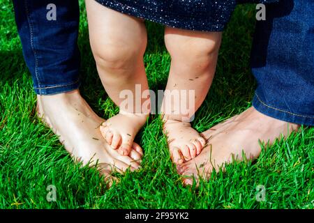 Gros plan des pieds de l'enfant debout sur les pieds de ses parents dans une herbe. Banque D'Images