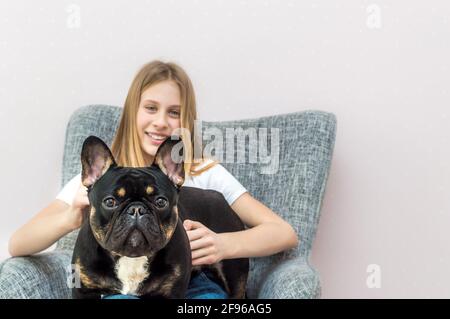 Adolescente assise dans une chaise à la maison avec elle Chien Bulldog français dans ses bras Banque D'Images