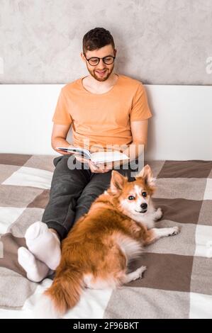 Un jeune homme lit un livre au lit avec son chien. Photo verticale Banque D'Images