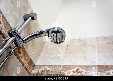 Intérieur d'une douche avec eau qui coule de la pomme de douche. Gouttelettes et humidité. Murs avec carreaux décorés. Hygiène et soins personnels Banque D'Images