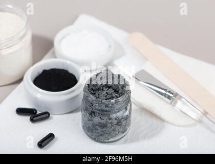 Ingrédients pour un masque facial au charbon de bois maison. Poudre de charbon de bois, huile de coco, argile cosmétique blanche. Concept beauté maison. Banque D'Images