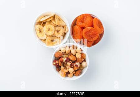 Abricots séchés, bananes séchées et un mélange de noix et de fruits confits en trois tasses sur fond clair. Vue de dessus. Le concept de naturel, sain s Banque D'Images