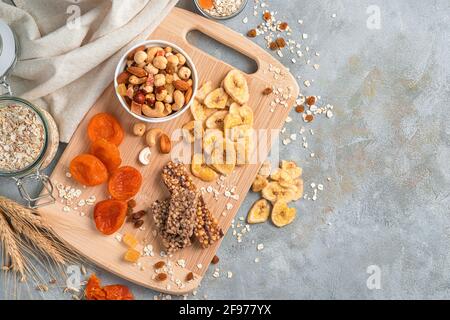 Un assortiment de fruits secs, de noix, de barres granola et de céréales sur fond gris avec espace à copier. Collations saines et naturelles. Banque D'Images