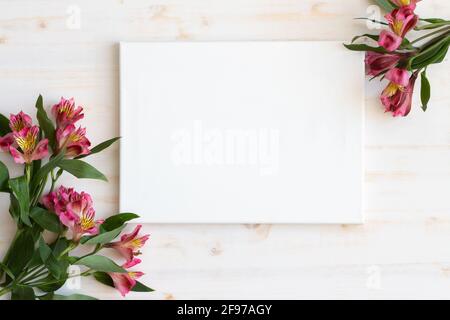 fleurs d'alstroemeria fraîches comme un cadre autour de toile blanche vierge avec espace de copie sur fond de bois blanc Banque D'Images