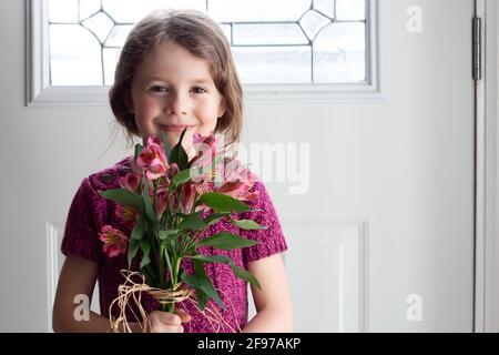 Jeune fille tenant un bouquet de fleurs d'alstroemerias rose frais, souriant et regardant l'appareil photo Banque D'Images