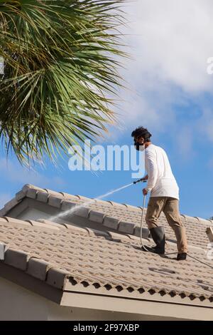 Homme lavant un toit de tuiles en Floride. Le jet haute pression élimine les feuilles, les brindilles, la saleté, les débris, la boue, mousses, spores de moisissures, lichens et algues. Banque D'Images