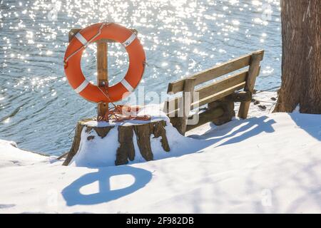 Hamm, Rhénanie-du-Nord-Westphalie, Allemagne - Ensoleillé paysage d'hiver dans la région de la Ruhr, glace et neige sur la Lippe, banc de parc avec bouée de sauvetage. Banque D'Images