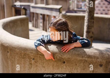 Une petite fille se penche sur un mur de pierre incurvé lors d'une journée ensoleillée et venteuse Banque D'Images