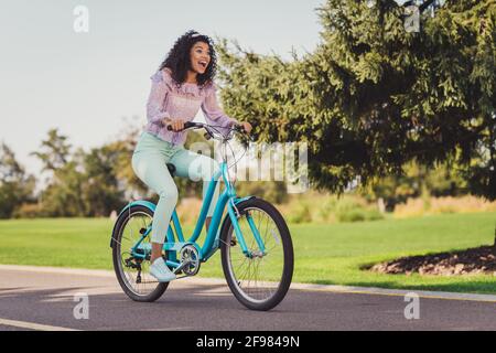 Photo pleine grandeur de brunette impressionnée femme à vélo de course haut pantalon lilas baskets dehors dans le parc Banque D'Images