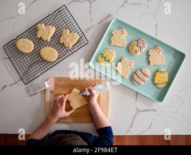 Enfant décorant des biscuits de Pâques sur un contre-coup blanc de dessus. Banque D'Images